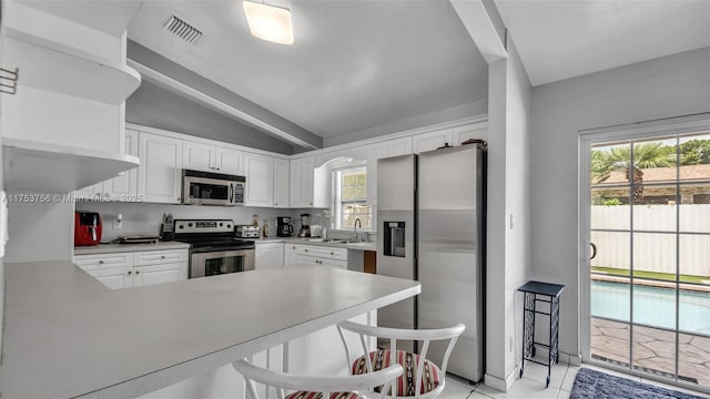 kitchen featuring stainless steel appliances, a peninsula, visible vents, white cabinetry, and vaulted ceiling