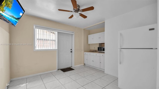 kitchen featuring light tile patterned floors, stainless steel microwave, freestanding refrigerator, and white cabinetry