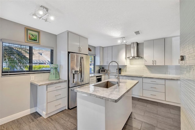 kitchen with a sink, visible vents, backsplash, stainless steel fridge with ice dispenser, and wall chimney exhaust hood