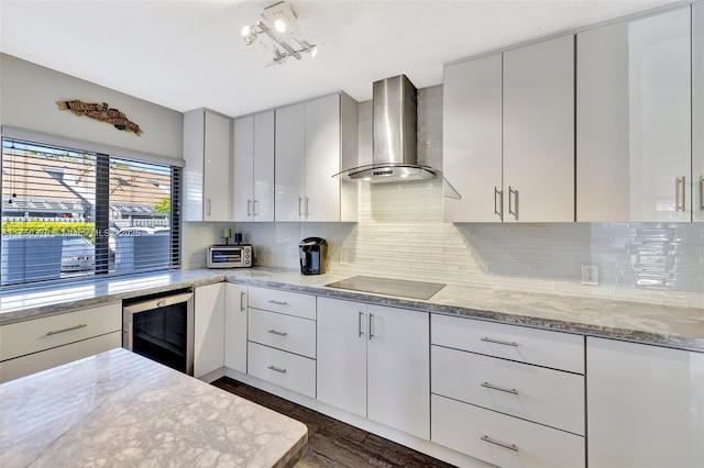 kitchen with black electric cooktop, a toaster, beverage cooler, wall chimney range hood, and backsplash