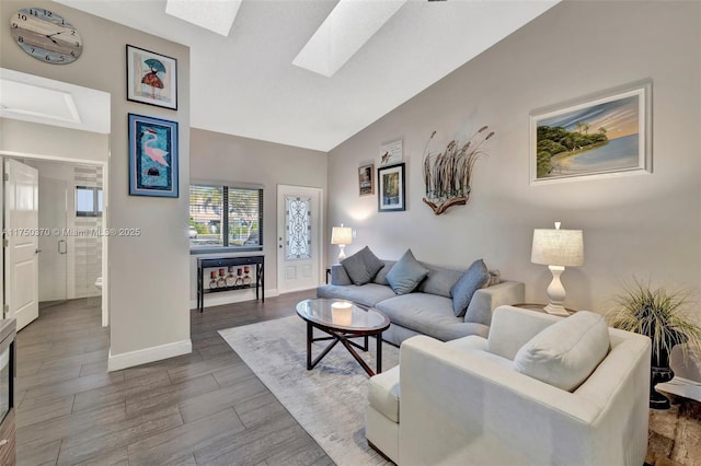 living area featuring lofted ceiling with skylight, baseboards, and wood finished floors