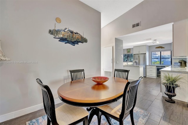 dining space featuring beverage cooler, lofted ceiling, visible vents, and baseboards