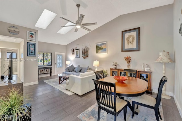 dining area featuring lofted ceiling with skylight, baseboards, a ceiling fan, and dark wood-type flooring