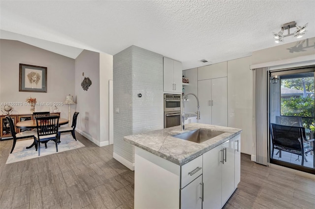 kitchen featuring a center island with sink, lofted ceiling, a textured ceiling, stainless steel double oven, and a sink