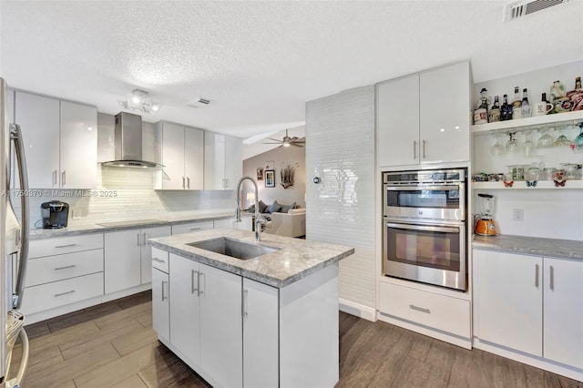 kitchen featuring dark wood finished floors, double oven, a sink, wall chimney exhaust hood, and black electric cooktop