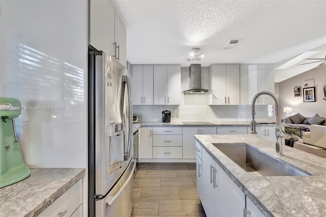 kitchen featuring black electric stovetop, a sink, decorative backsplash, wall chimney exhaust hood, and stainless steel fridge