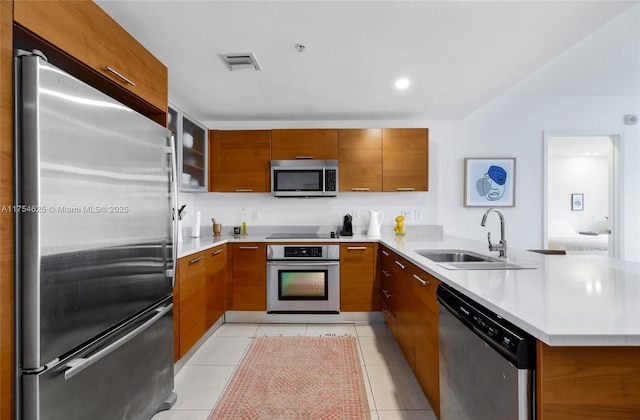 kitchen with visible vents, appliances with stainless steel finishes, brown cabinetry, a sink, and a peninsula