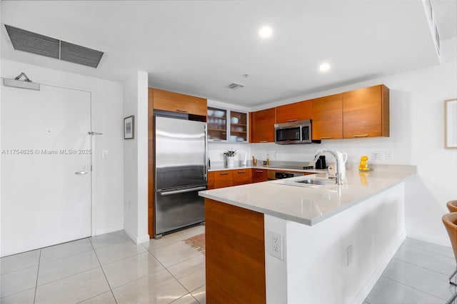 kitchen featuring visible vents, brown cabinetry, appliances with stainless steel finishes, a peninsula, and light countertops