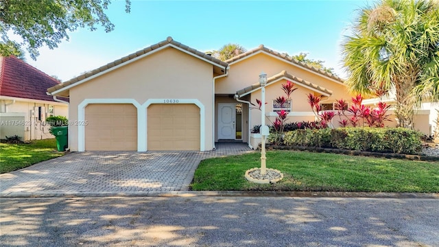 view of front of property with an attached garage, a tile roof, decorative driveway, stucco siding, and a front lawn