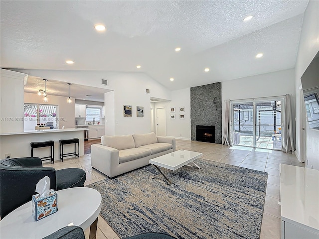 living area featuring vaulted ceiling, a textured ceiling, a fireplace, and light tile patterned flooring