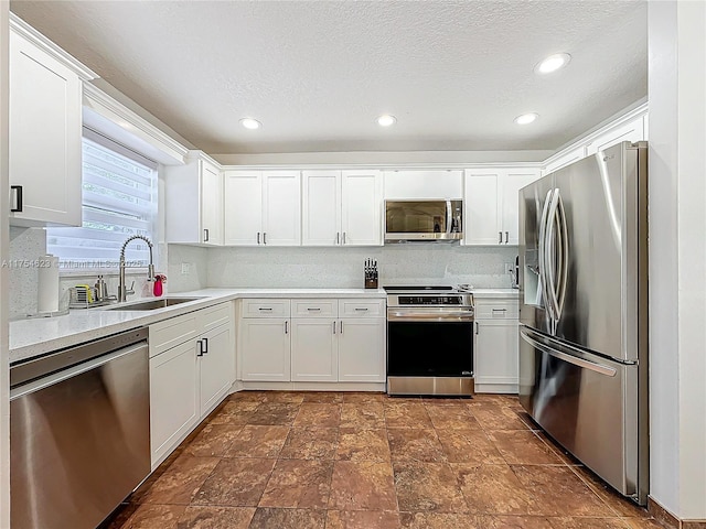 kitchen with stainless steel appliances, light countertops, backsplash, white cabinets, and a sink