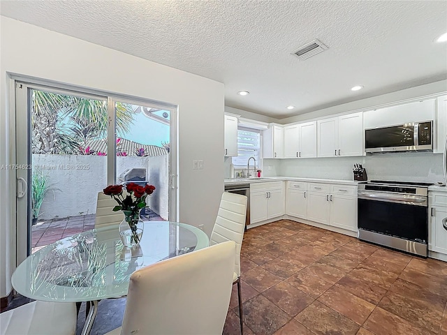 kitchen with stainless steel appliances, light countertops, visible vents, white cabinetry, and a sink