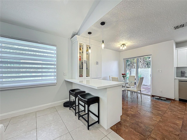 kitchen with a textured ceiling, a peninsula, white cabinets, light countertops, and pendant lighting