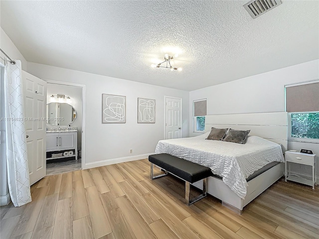 bedroom featuring baseboards, visible vents, a textured ceiling, and light wood finished floors