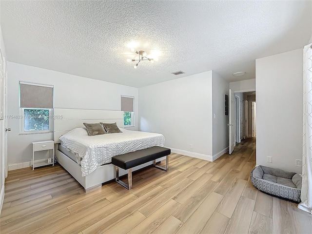 bedroom featuring a textured ceiling, light wood finished floors, visible vents, and baseboards