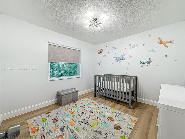 bedroom with a textured ceiling, a crib, light wood-type flooring, and baseboards