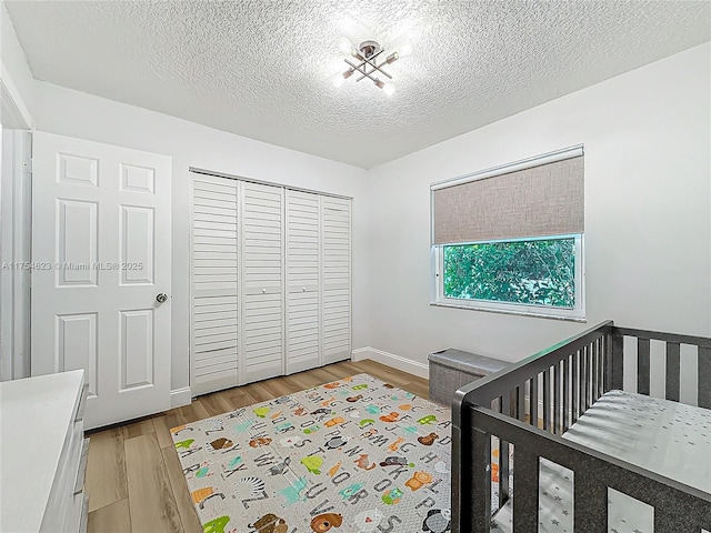 bedroom featuring a closet, a textured ceiling, light wood-type flooring, a crib, and baseboards