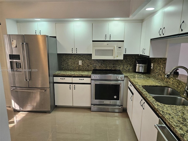 kitchen featuring white cabinets, appliances with stainless steel finishes, dark stone countertops, a sink, and backsplash