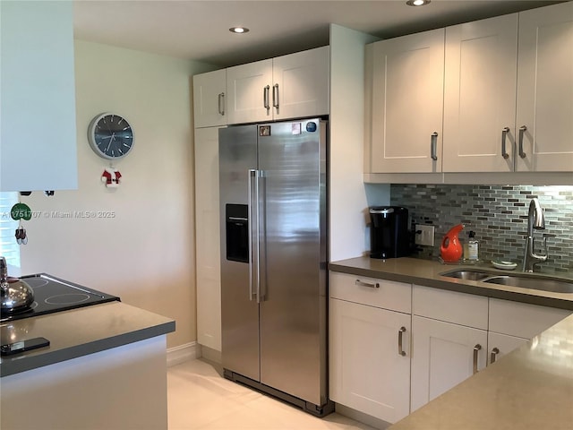 kitchen with stainless steel fridge, a sink, backsplash, and white cabinetry