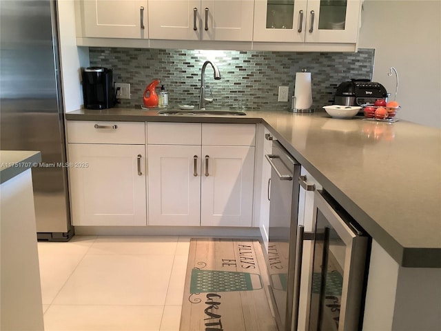 kitchen featuring a sink, white cabinetry, stainless steel refrigerator, decorative backsplash, and glass insert cabinets