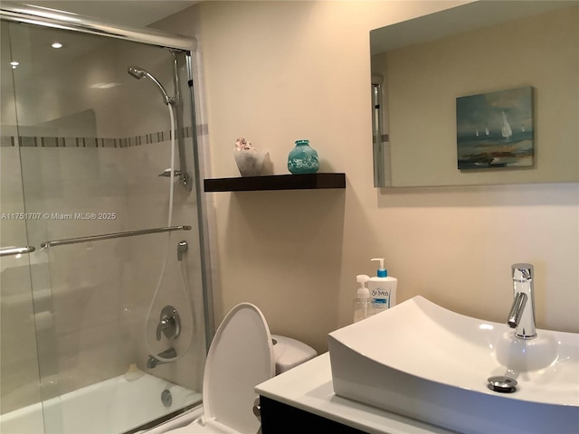 full bathroom with combined bath / shower with glass door, vanity, and toilet