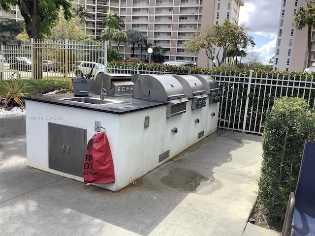 exterior space with a grill, a sink, an outdoor kitchen, and fence