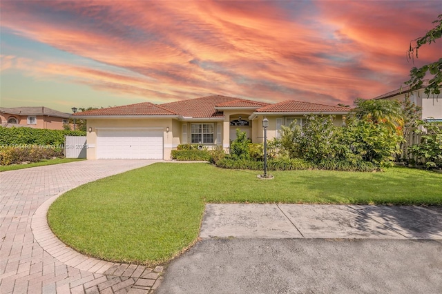 mediterranean / spanish-style home featuring decorative driveway, stucco siding, a lawn, a garage, and a tiled roof