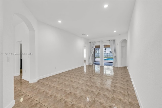 unfurnished room featuring baseboards, arched walkways, and recessed lighting