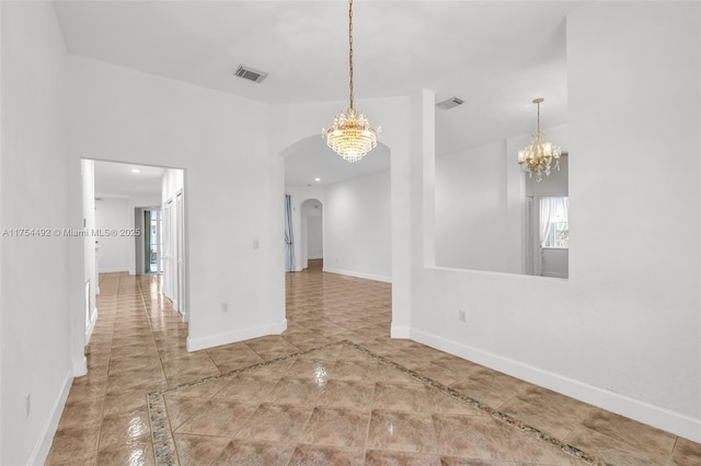 unfurnished room featuring a chandelier, arched walkways, visible vents, and baseboards