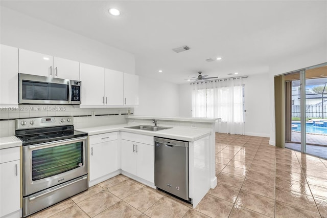 kitchen featuring tasteful backsplash, light countertops, appliances with stainless steel finishes, a sink, and a peninsula