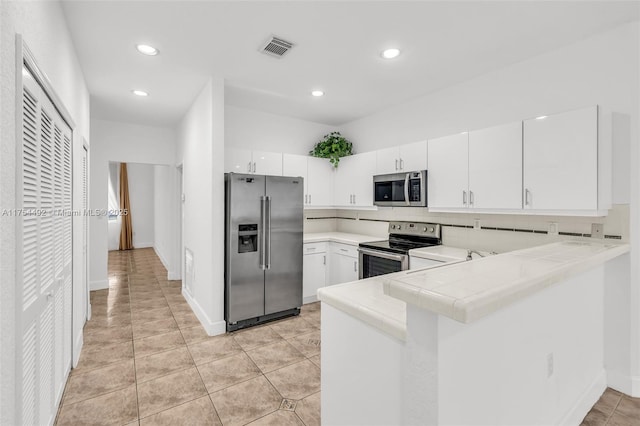 kitchen featuring tasteful backsplash, visible vents, tile counters, appliances with stainless steel finishes, and a peninsula