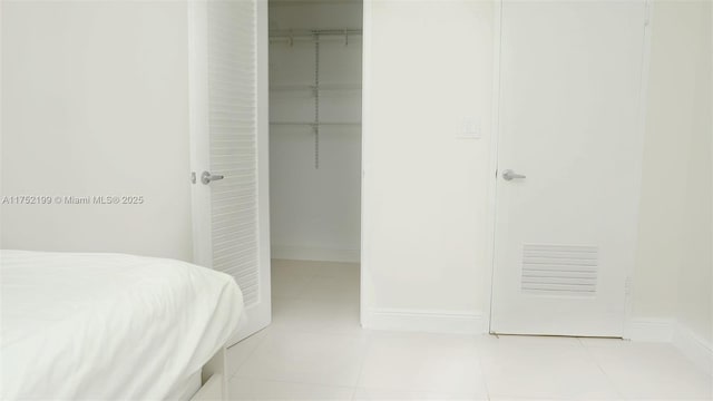 tiled bedroom with a closet, a walk in closet, and baseboards