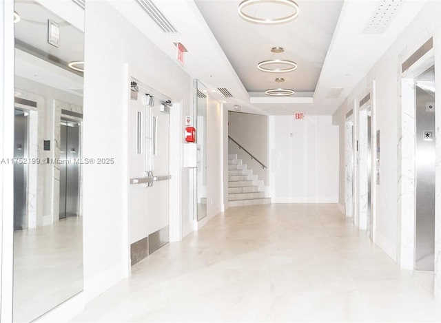 hallway featuring a tray ceiling, elevator, visible vents, and stairway