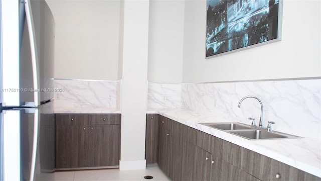 kitchen featuring freestanding refrigerator, backsplash, a sink, and dark brown cabinetry