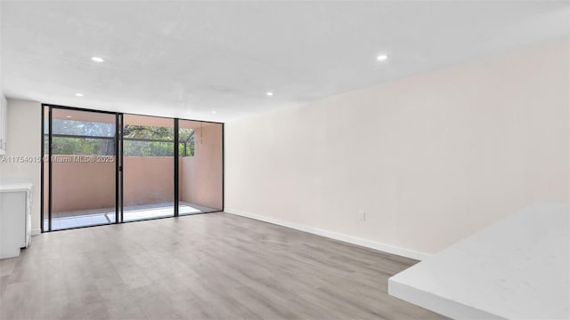 empty room with expansive windows, light wood finished floors, recessed lighting, and baseboards