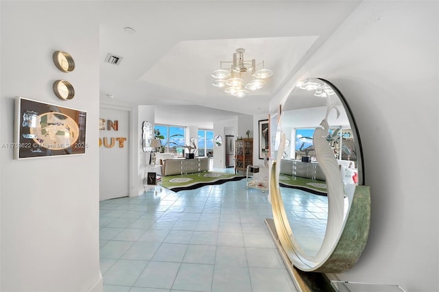 hall with light tile patterned floors, lofted ceiling, visible vents, a tray ceiling, and an inviting chandelier