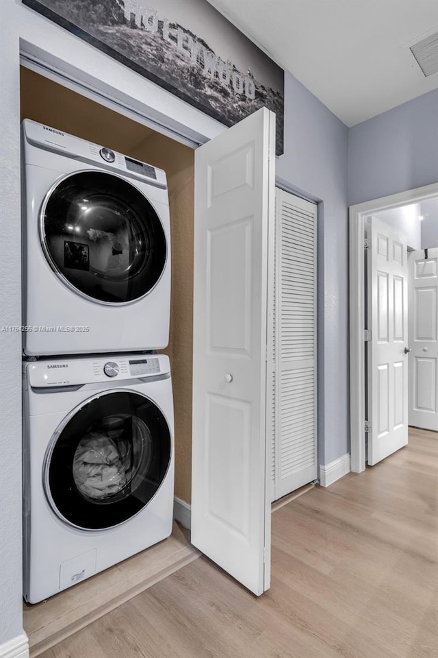 clothes washing area featuring stacked washer and clothes dryer, visible vents, light wood-style floors, laundry area, and baseboards