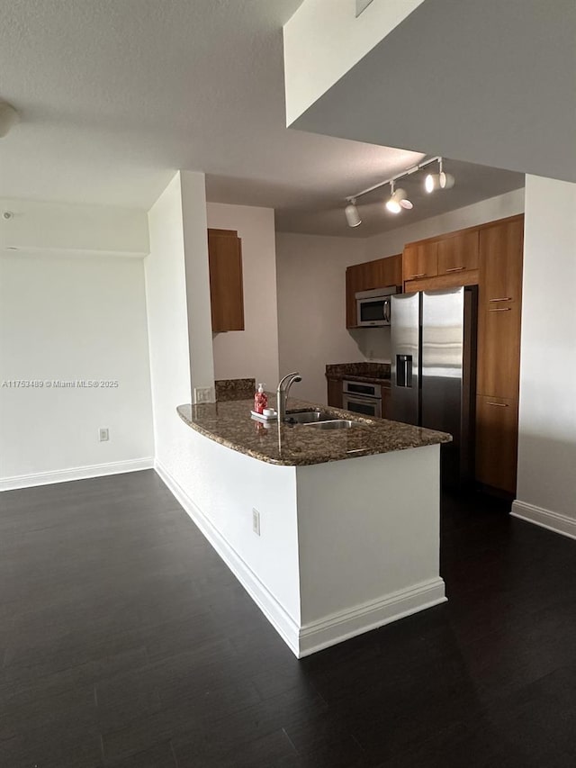 kitchen featuring dark wood-style floors, appliances with stainless steel finishes, brown cabinets, a peninsula, and a sink