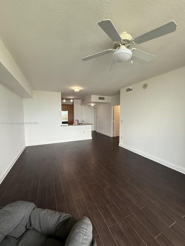 unfurnished living room with dark wood-style floors, a textured ceiling, and baseboards