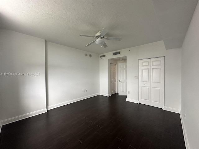 unfurnished bedroom with baseboards, a textured ceiling, visible vents, and dark wood-type flooring