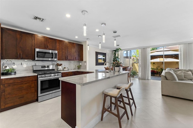 kitchen with visible vents, appliances with stainless steel finishes, open floor plan, a sink, and backsplash