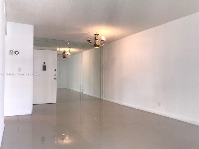 tiled empty room featuring a chandelier and a textured ceiling