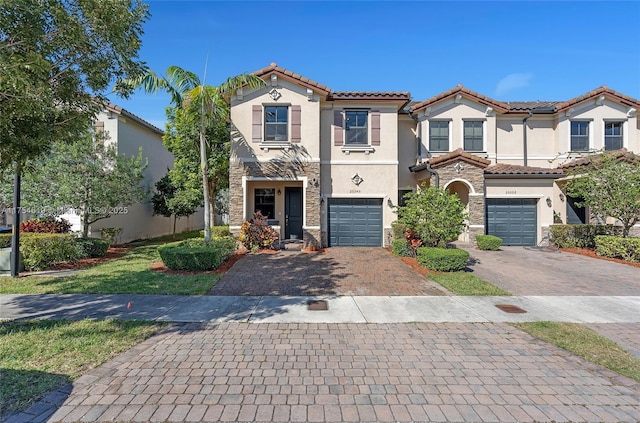 mediterranean / spanish home with stone siding, decorative driveway, an attached garage, and stucco siding