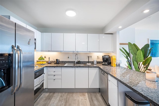 kitchen with appliances with stainless steel finishes, dark stone counters, white cabinets, and a sink