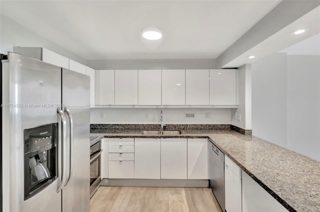 kitchen featuring appliances with stainless steel finishes, white cabinetry, a sink, dark stone countertops, and light wood-type flooring