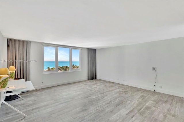 unfurnished living room with light wood-style floors, a water view, and baseboards