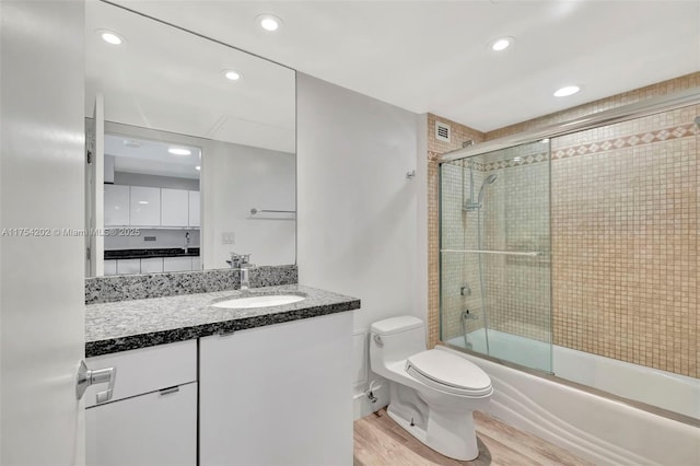 full bath featuring toilet, enclosed tub / shower combo, wood finished floors, vanity, and recessed lighting