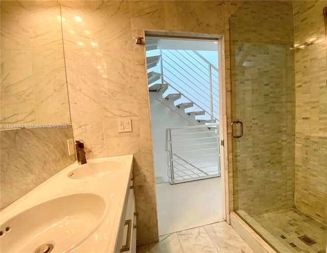 bathroom featuring marble finish floor, a stall shower, a sink, and tile walls