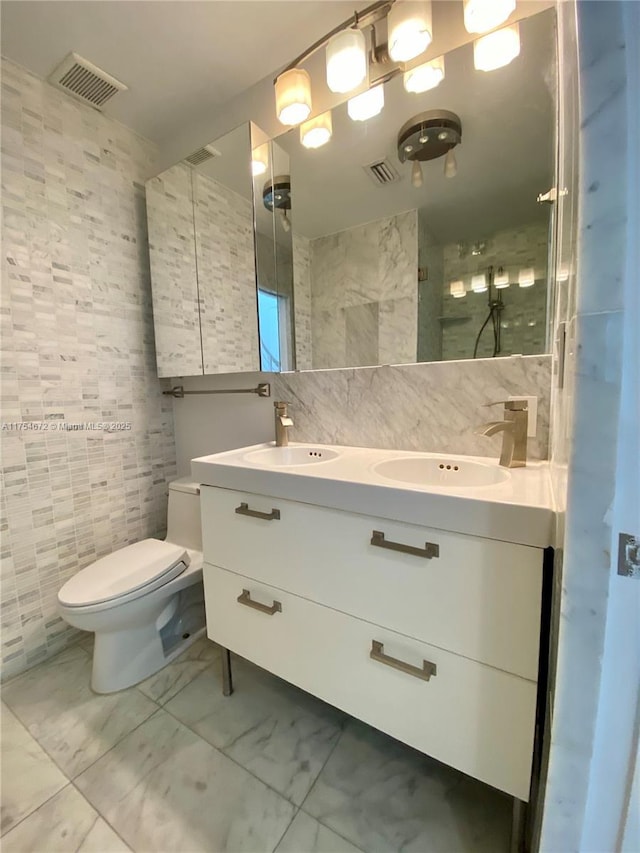 bathroom featuring visible vents, marble finish floor, a sink, and tile walls