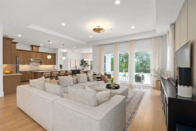 living area with light wood-style floors, visible vents, a raised ceiling, and recessed lighting